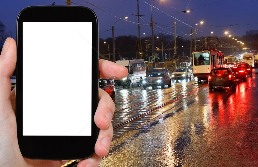 旅行概念手持智能机在夜里按背景截断屏幕在城市街道上湿透图片