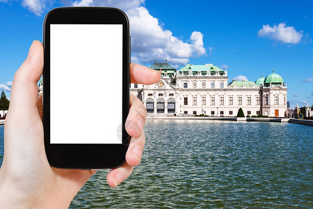 旅行概念游客用智能手机拍摄维也纳上贝尔韦代雷宫用空白广告标志的屏剪图片