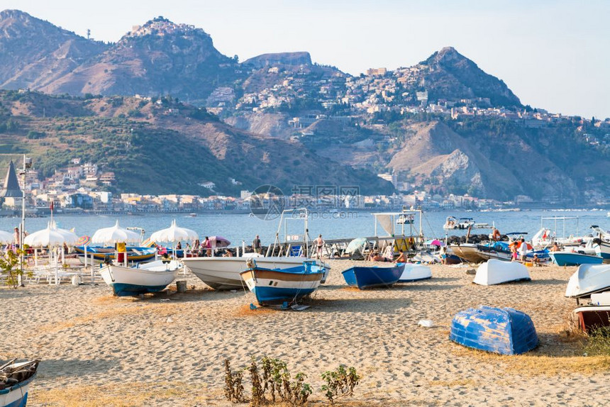 前往意大利西里夏季在GiardiniNaxos镇旧港口海滩上的船只和Taormina市角斗篷的景色图片