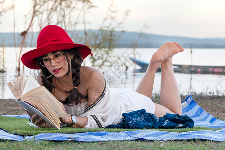 美丽的女人快乐微笑和阅读书籍在湖边的田地上快乐微笑图片