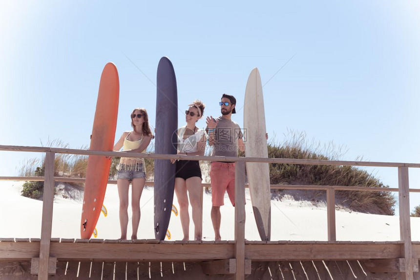 男孩女少年冲浪者板站在木制通道上看着海滩的浪图片