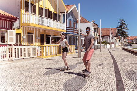 科斯塔诺瓦在葡萄牙阿维罗Aveiro典型的科斯塔新屋附近玩滑板的年轻活跃夫妇背景