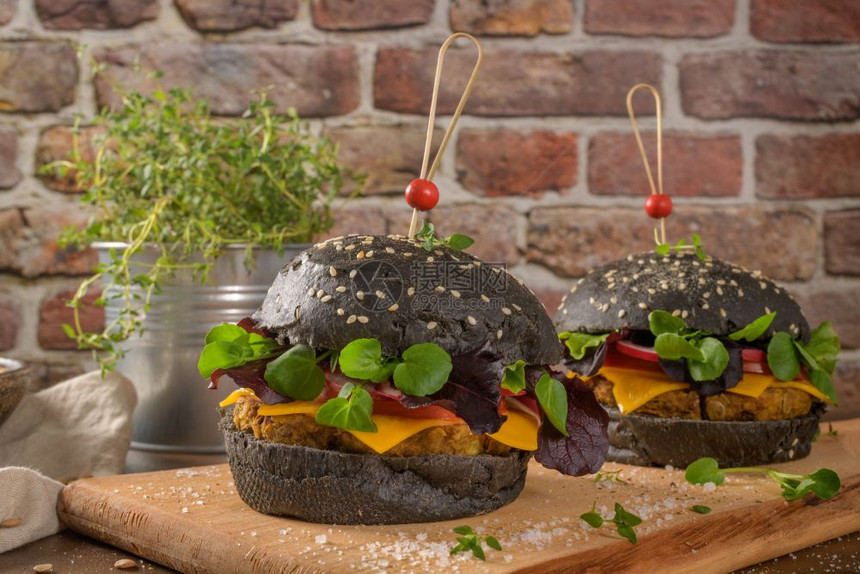 美味的烤肉汉堡扁豆干西红柿和百草枯黑面包在木制顶上图片