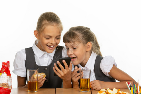 两个女学生在休息时间观看一个视频在电话上吃肝和橙子喝果汁图片