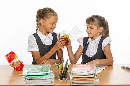 两个有趣的女学生坐在桌边喝果汁和撞上眼镜图片