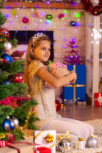 10岁女孩坐在圣诞树上拥抱礼物图片