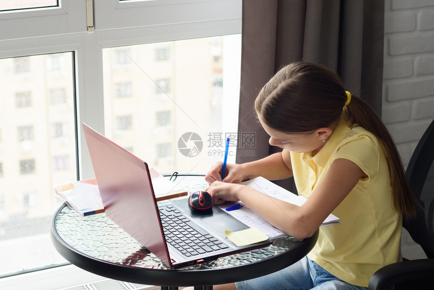 女孩在一个房间里做功课坐在窗边的桌子上图片