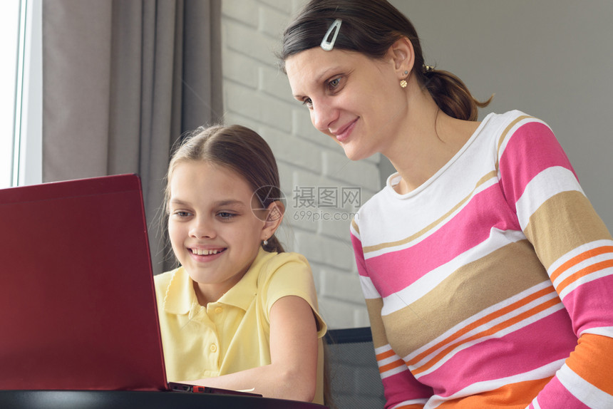 快乐的女孩和坐在桌子上看笔记本电脑屏幕图片
