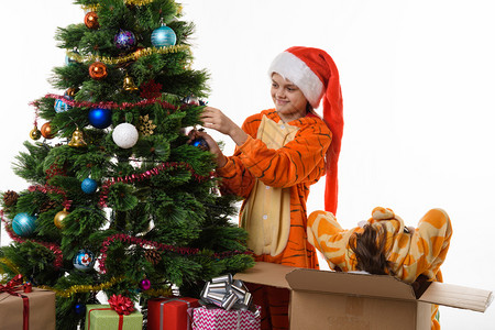 一个女孩把球挂在圣诞树上另一个女孩带着头爬进盒子里背景图片
