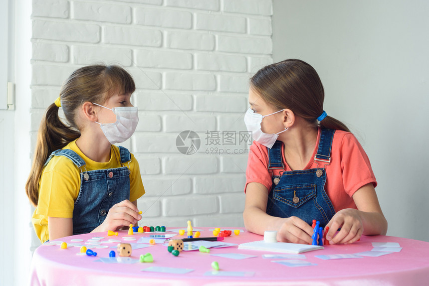 两个女孩在检疫游戏桌上玩时戴保护医疗面具图片
