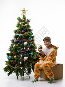 女孩坐在盒子上储存圣诞装饰品手里握着球图片