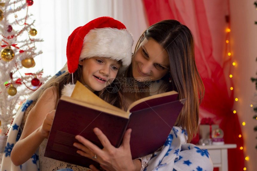 带着孩子的女在装饰圣诞节房间读一本书图片
