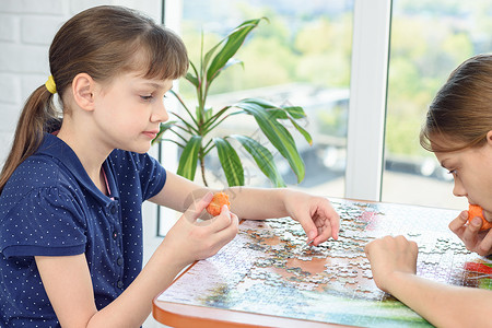 两个女孩在桌边收集拼图吃胡萝卜高清图片