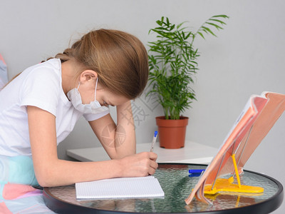 戴着医疗面具的女孩在床前桌子上做功课图片