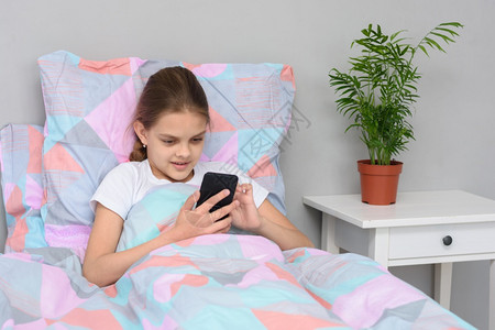 女孩躺在床上时通过手机与朋友进行在线交流图片