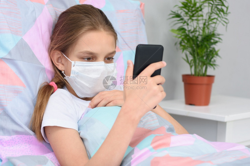 身戴医疗面具的女孩躺在床上看着电话屏幕图片