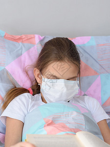 生病的女孩在阅读一本书时睡着了并用医疗面具蒙住她的脸图片