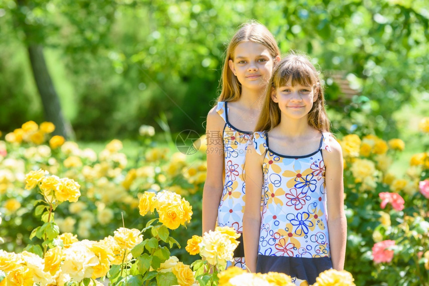 两个女孩站在美丽的花园玫瑰朵中图片