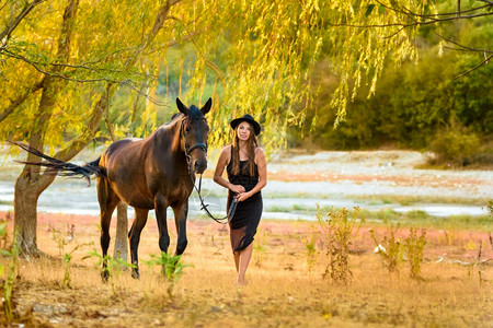 穿漂亮黑裙子的女孩戴着黑帽子骑马走过田地图片
