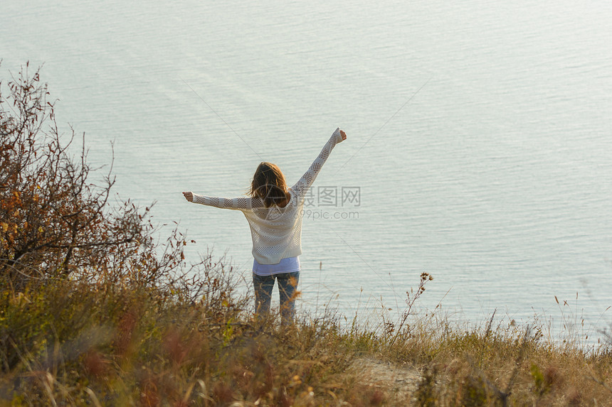 快乐的姑娘举起手来享受海景从后面看风图片