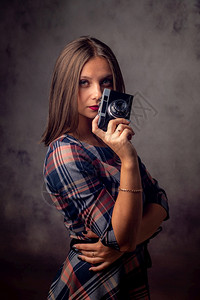 女孩摄影师手里握着旧相机摄影棚拍在灰色背景上图片