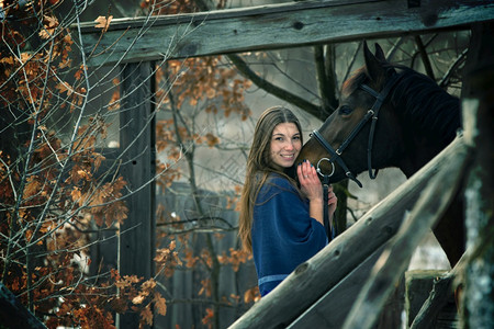 一个穿蓝衣服的漂亮女孩站在一匹马旁边站在木制建筑背景的上图片