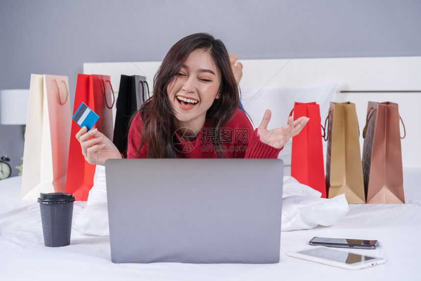 开心的女士使用笔记本电脑在床上网购物图片
