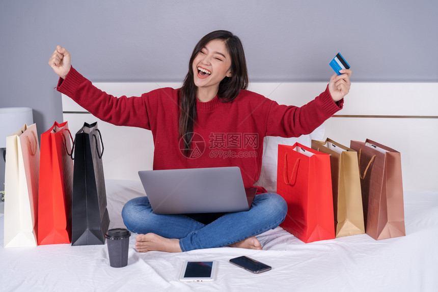 开心的女士使用笔记本电脑在床上网购物图片