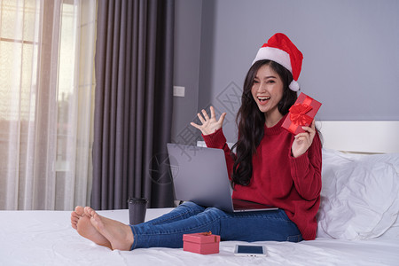 使用笔记本电脑和在床上持有圣诞礼物的幸福妇女图片