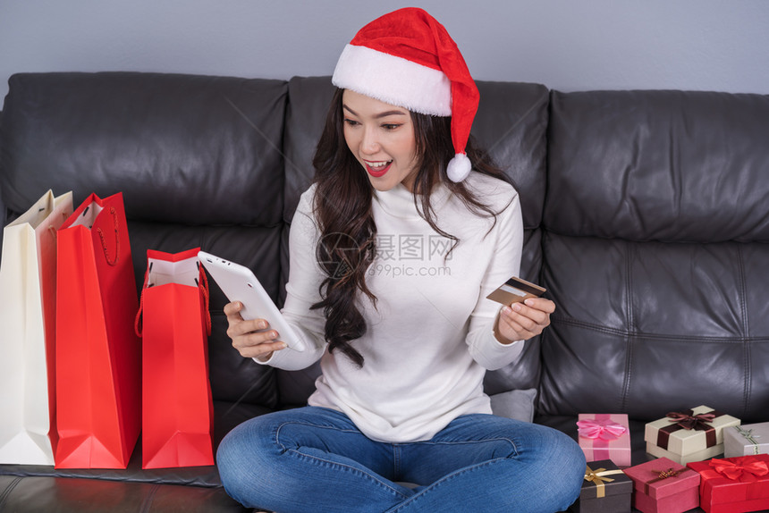 妇女在线购买圣塔帽诞礼物在客厅用数码平板电脑购买图片