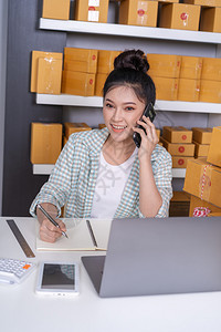 青年女企业家与移动电话客户交谈和在家庭办公室撰写产品订单图片