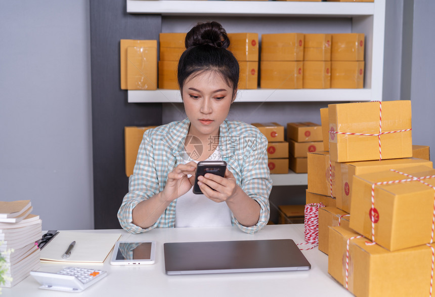 在家办公用智能手机小型在线企业主工作的妇女和检查产品订单图片