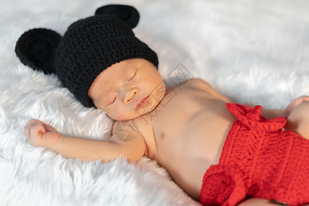 米奇老鼠穿着老鼠服装的新生婴儿睡在毛皮床上背景