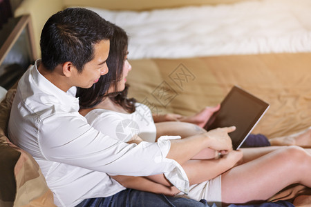 与丈夫一起怀孕的妇女在床上使用数字平板电脑图片