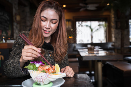 色味俱佳寿司女人在餐厅里吃鲑鱼生辣色沙拉背景