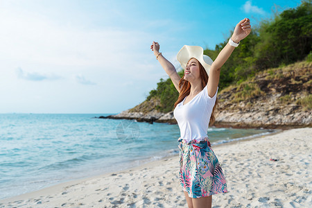 戴帽子的妇女手举高站在海边的图片
