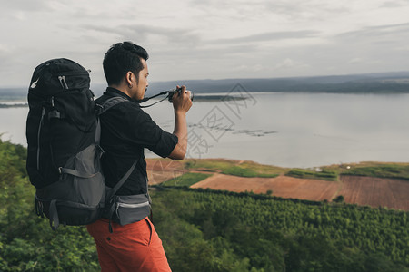 背着包的男旅行者使用相机拍摄照片在悬崖边缘岩石山顶背景图片