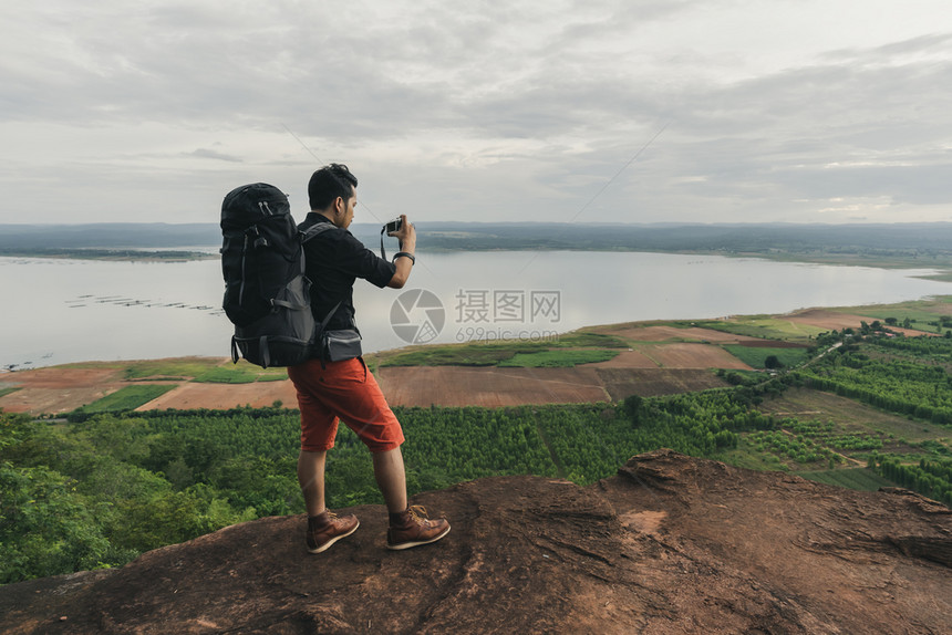 背着包的男旅行者使用相机拍摄照片在悬崖边缘岩石山顶图片