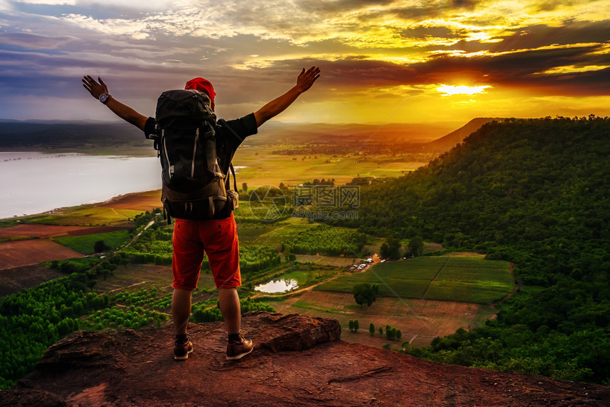 欢乐的徒步男子手势在悬崖边缘举起手臂在日落时岩石山顶图片