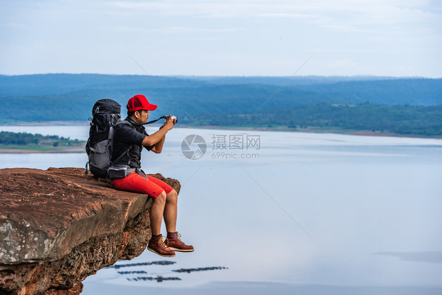 背着包的男旅行者使用相机拍摄照片在悬崖边缘岩石山顶图片