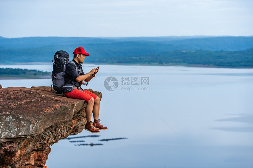 坐在悬崖边缘岩石山顶的悬崖边缘使用智能手机的人图片