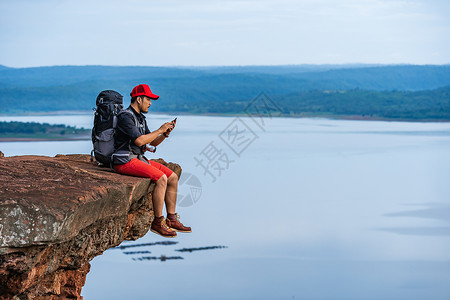 坐在悬崖边缘岩石山顶的悬崖边缘使用智能手机的人图片