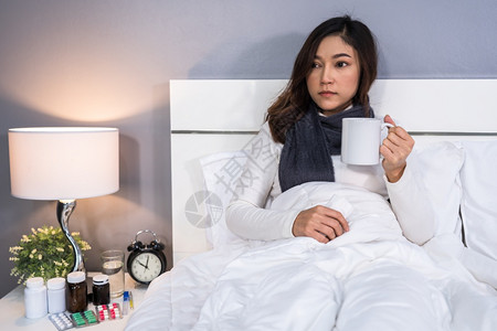 生病的妇女在床上喝一杯咖啡热水图片