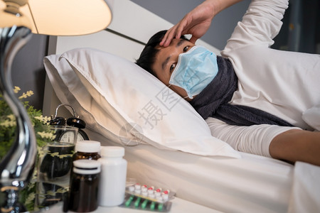 戴医疗面具的有病男子头痛在床上患有疾和发烧有冠状新冠大流行概念图片