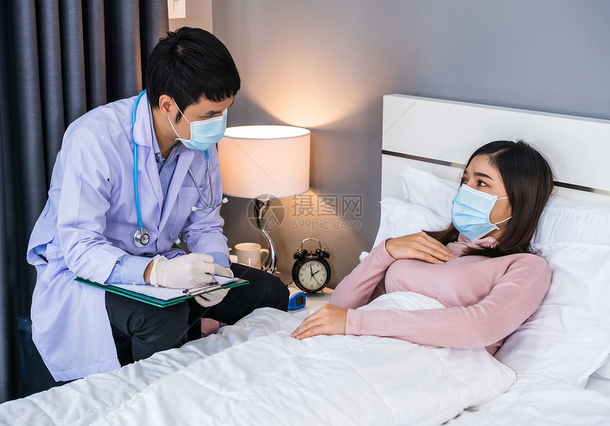 医生在剪贴板上与床的女病人交谈和撰写诊断时人们必须佩戴防冠状新冠大流行的医疗面具图片