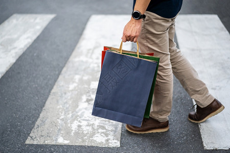 持有购物袋的男子在城市横过街上行走图片