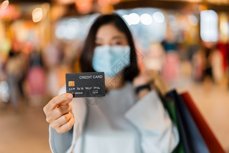 在购物中心佩戴医疗面具的年轻妇女信用卡以防止科罗纳新冠大流行图片