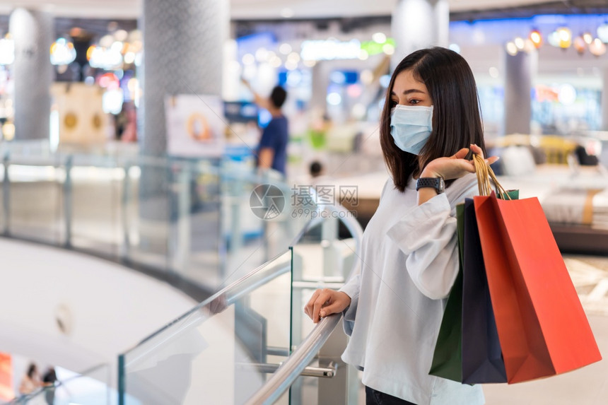 年轻妇女在商场用包购物并戴医疗面具以防止科罗纳新冠大流行图片
