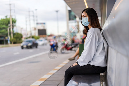 年轻妇女在市街公共汽车站等并戴面罩保护传播新正常概念的冠状新冠流行病图片
