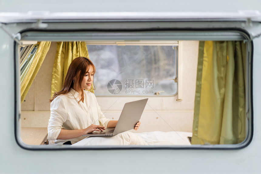 青年妇女用膝上型计算机在露营车RV面包摩托之家的床铺上使用笔记本电脑图片